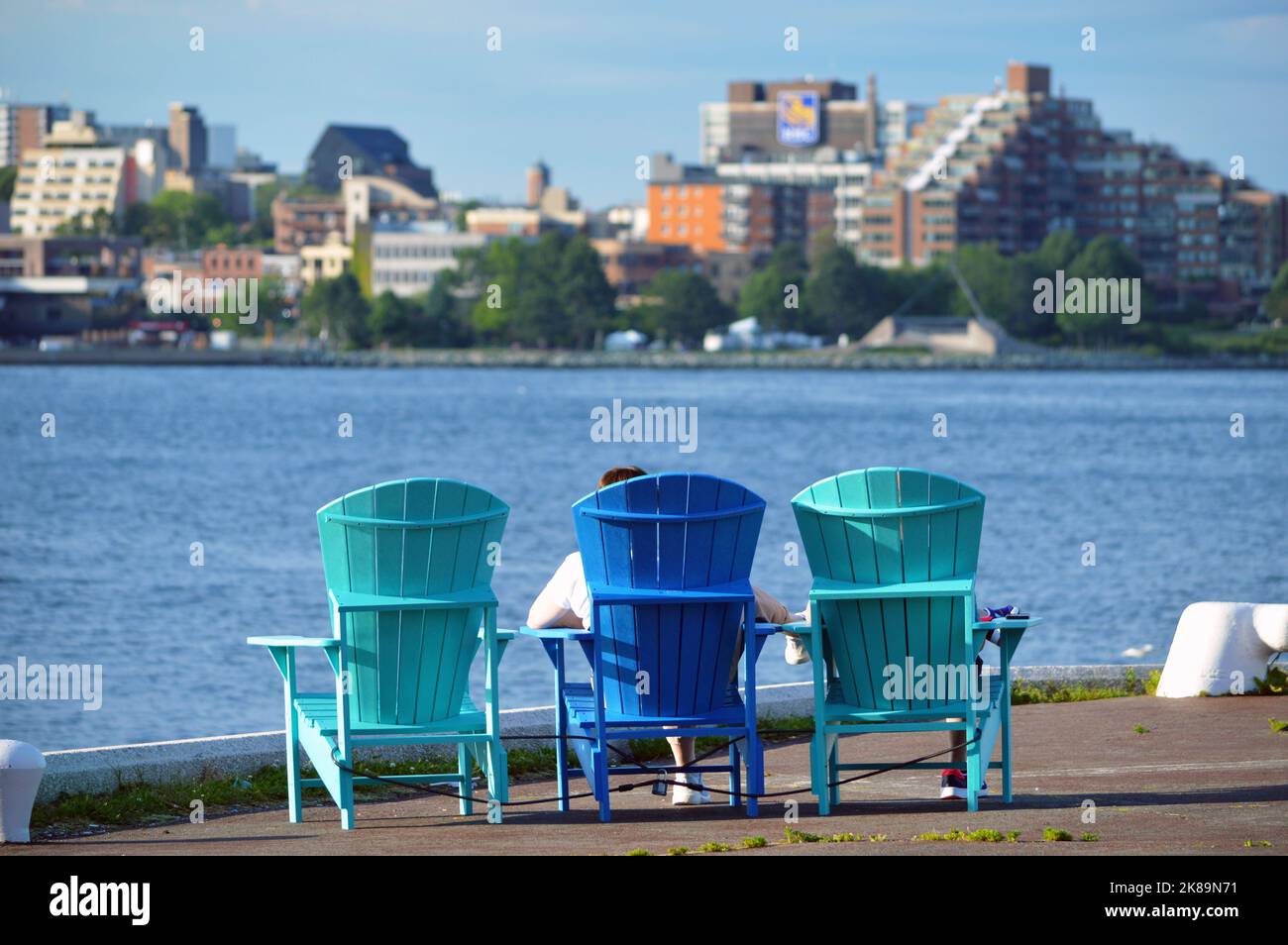 People lounge in colourful seating, Adirondack chairs (Muskoka chairs), on the urban waterfront of the Atlantic Canadian city of Halifax, Nova Scotia Stock Photo