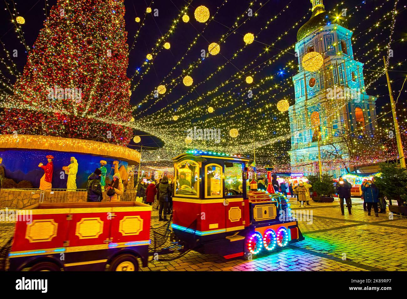 KYIV, UKRAINE - DECEMBER 28, 2021: St Sophia Square with Christmas Fair stalls, shiny tourist train, main Christmas Tree and medieval bell tower of St Stock Photo