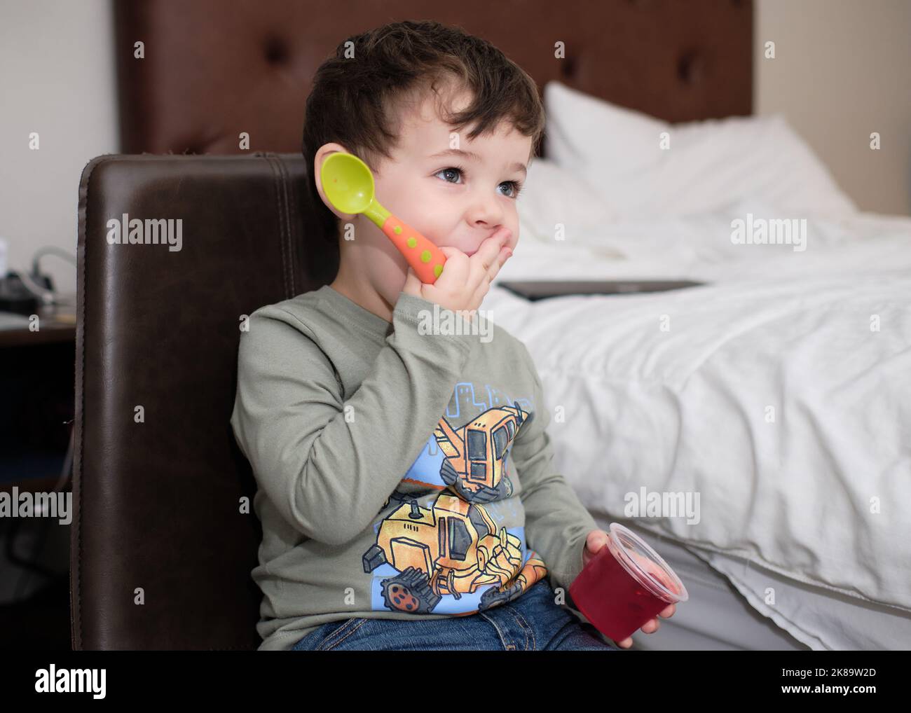 cute expressive young boy is eating a gelatin snack while watcching TV in a hotel room Stock