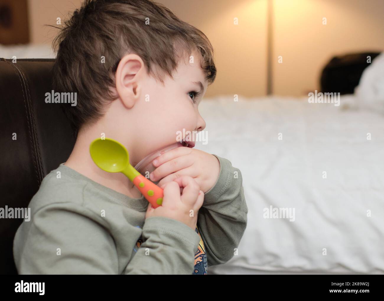 cute expressive young boy is eating a gelatin snack while watcching TV in a hotel room Stock