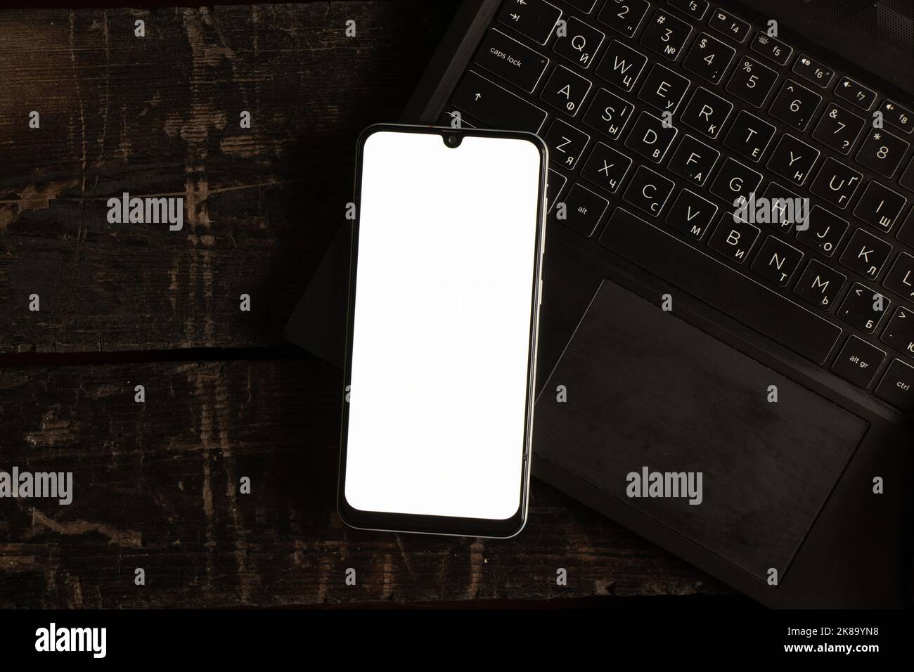 a phone with a white screen lies on a black laptop on a table, a phone template with a white screen Stock Photo