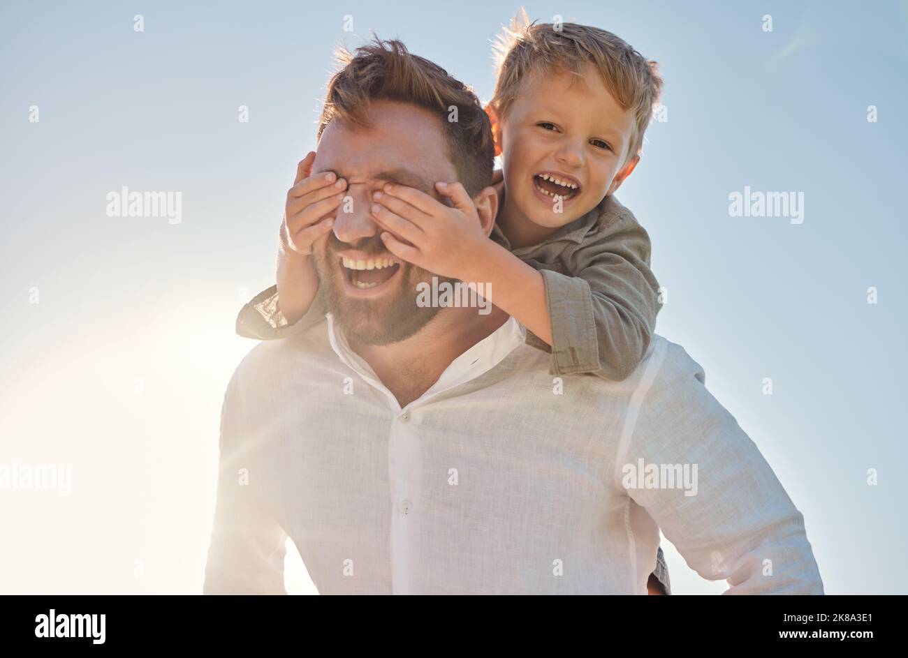 Dad, child and piggy back with covering eyes for game, playing and funny time in sunshine with love. Sun, sky and family with bonding, father and kid Stock Photo