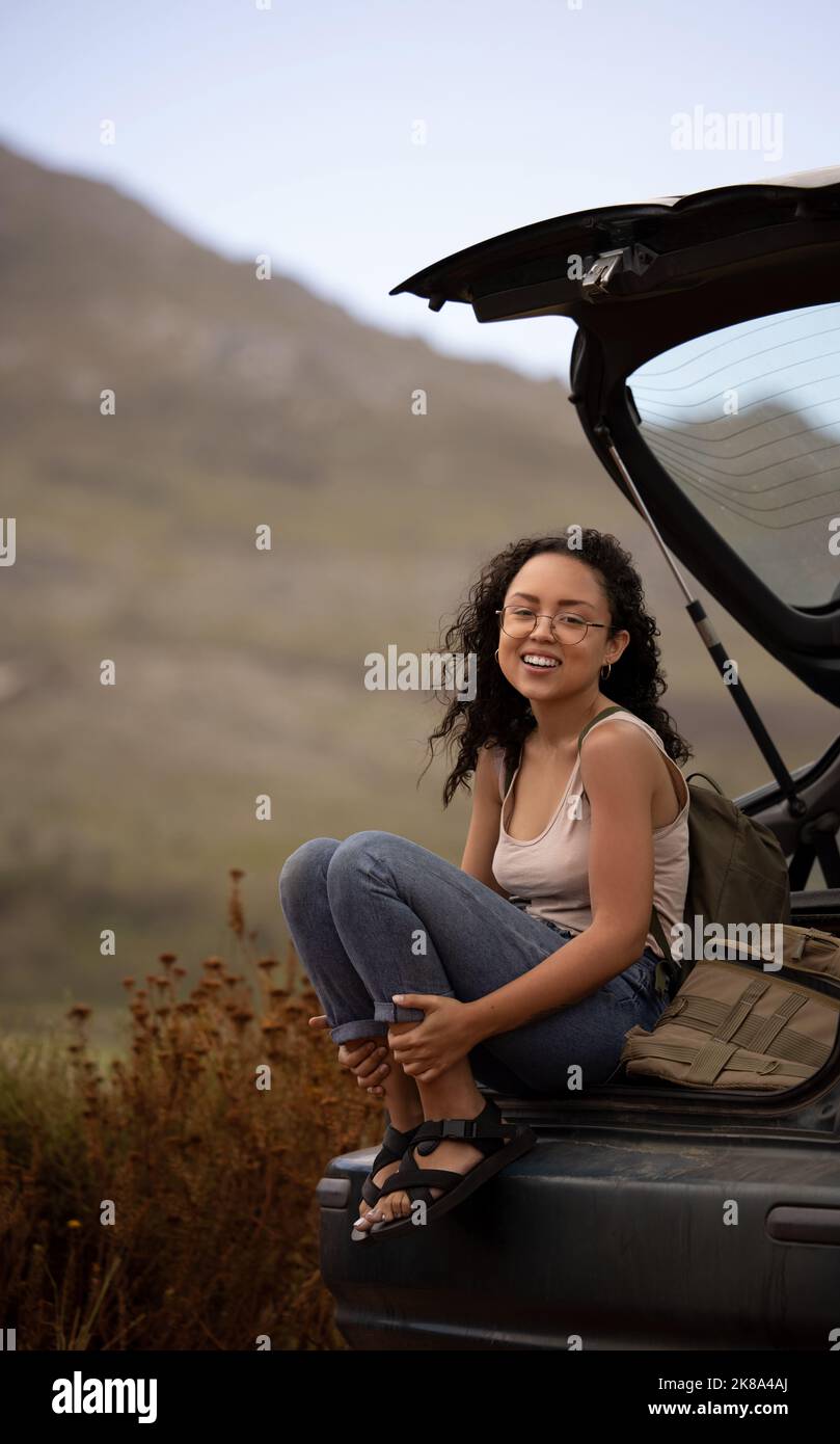 A roadtrip is not about the destination, its about the journey. a young woman sitting on a car while on a stop during a road trip. Stock Photo