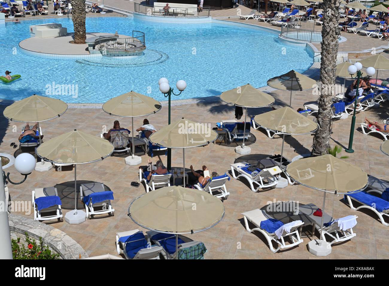 View from terrace of hotel on the people relaxing on plastic deck chairs under beach umbrellas. Stock Photo