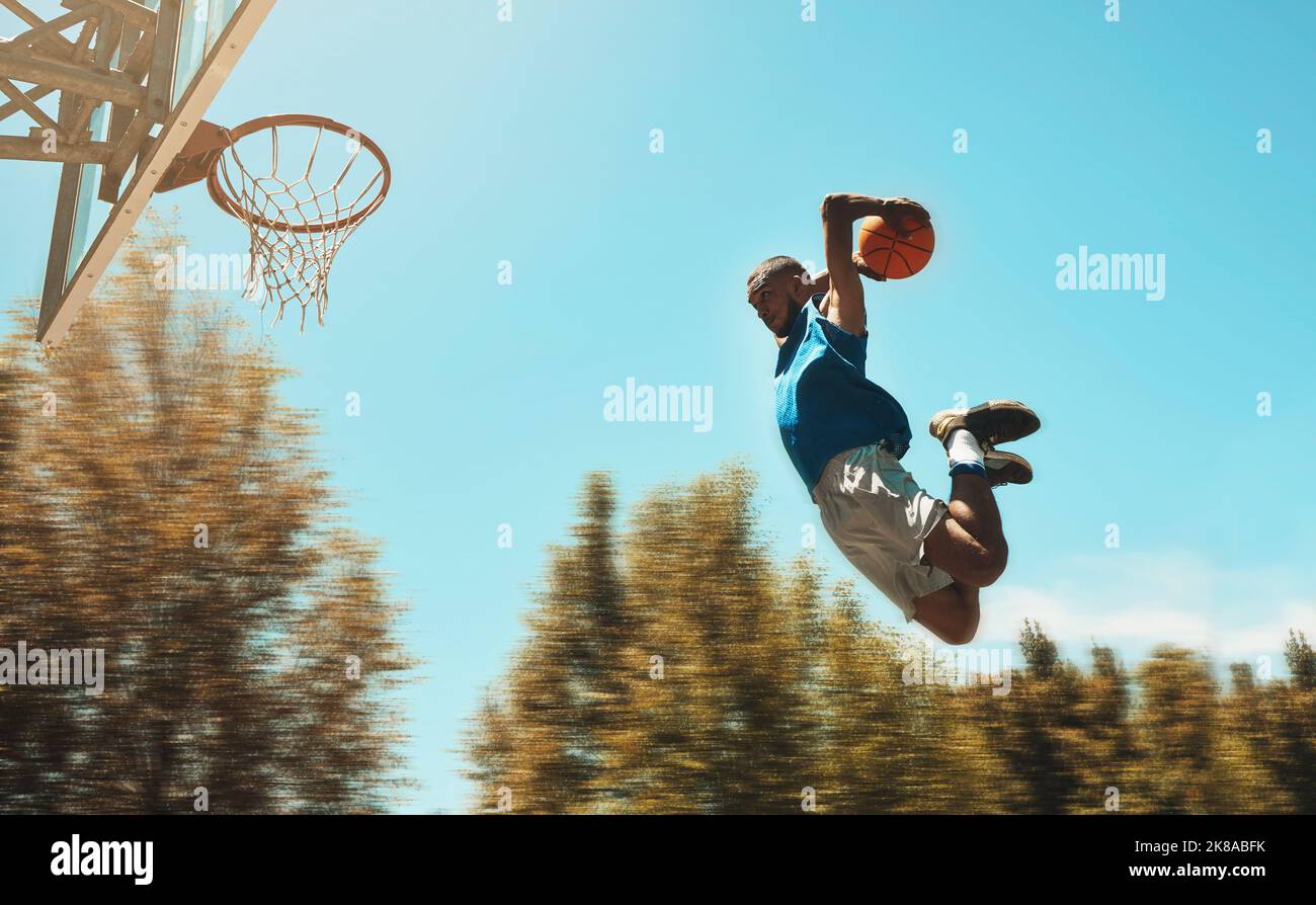 Basketball, sports and dunk with a man athlete jumping or flying through the air to score while playing on an outdoor court against the sky. Sport Stock Photo
