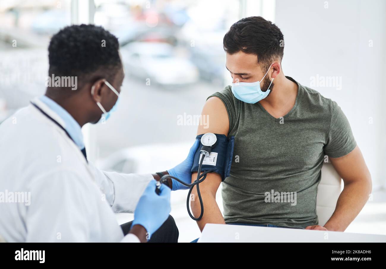 Hypertension happens, regular screening helps. a doctor examining a young man with a blood pressure gauge. Stock Photo