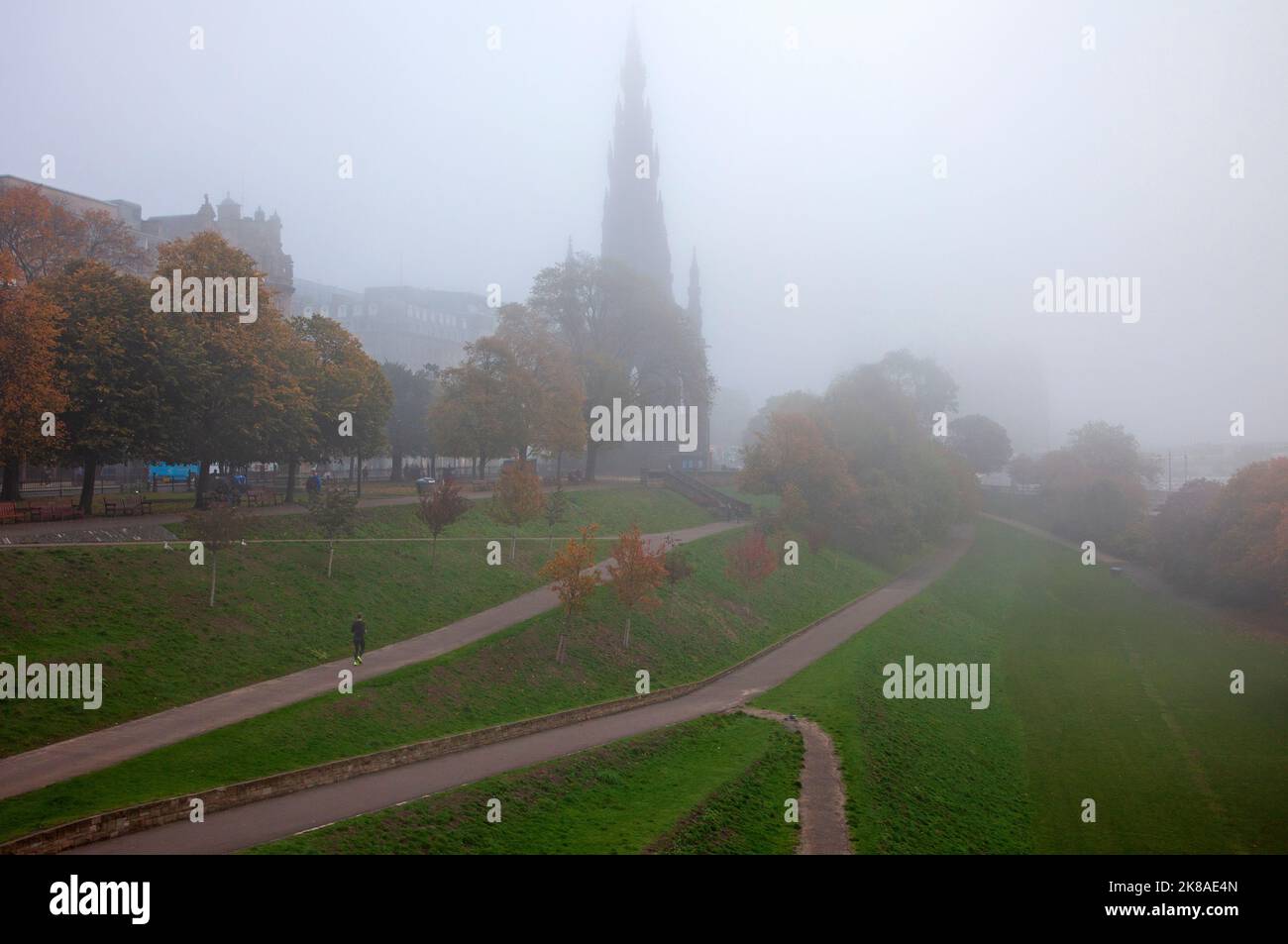 Edinburgh city centre, Scotland, UK. 22nd October 2022. UK Government, Queen Elizabeth House building. Thick fog covered the city overnight and early morning until rain came in mid morning. Temperature 11 degrees centigrade. Pictured: Lone jogger runs along path in Princes Street Gardens East. Credit: Arch White/alamy live news. Stock Photo