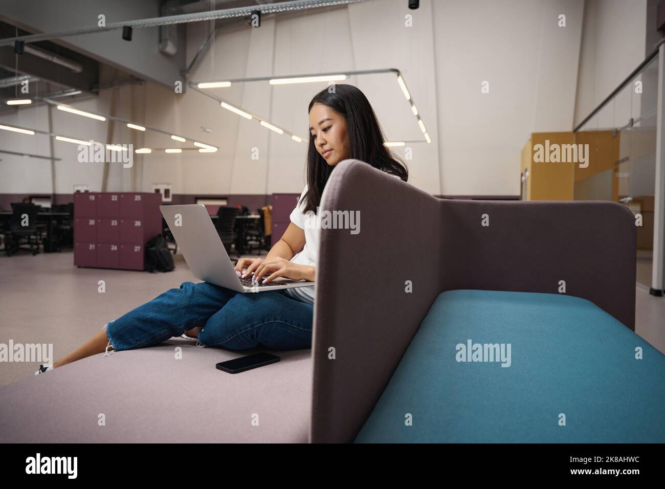 Concentrated female is sitting on the couch in the open workspace Stock ...