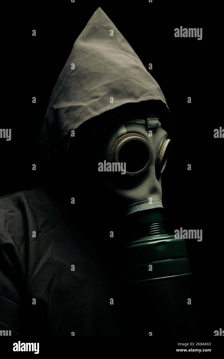 A scary man in a cloak wearing a gas mask. Dark background. Stock Photo