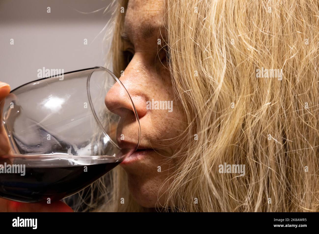 Young blonde woman drinking from a crystal glass with red wine. Concept