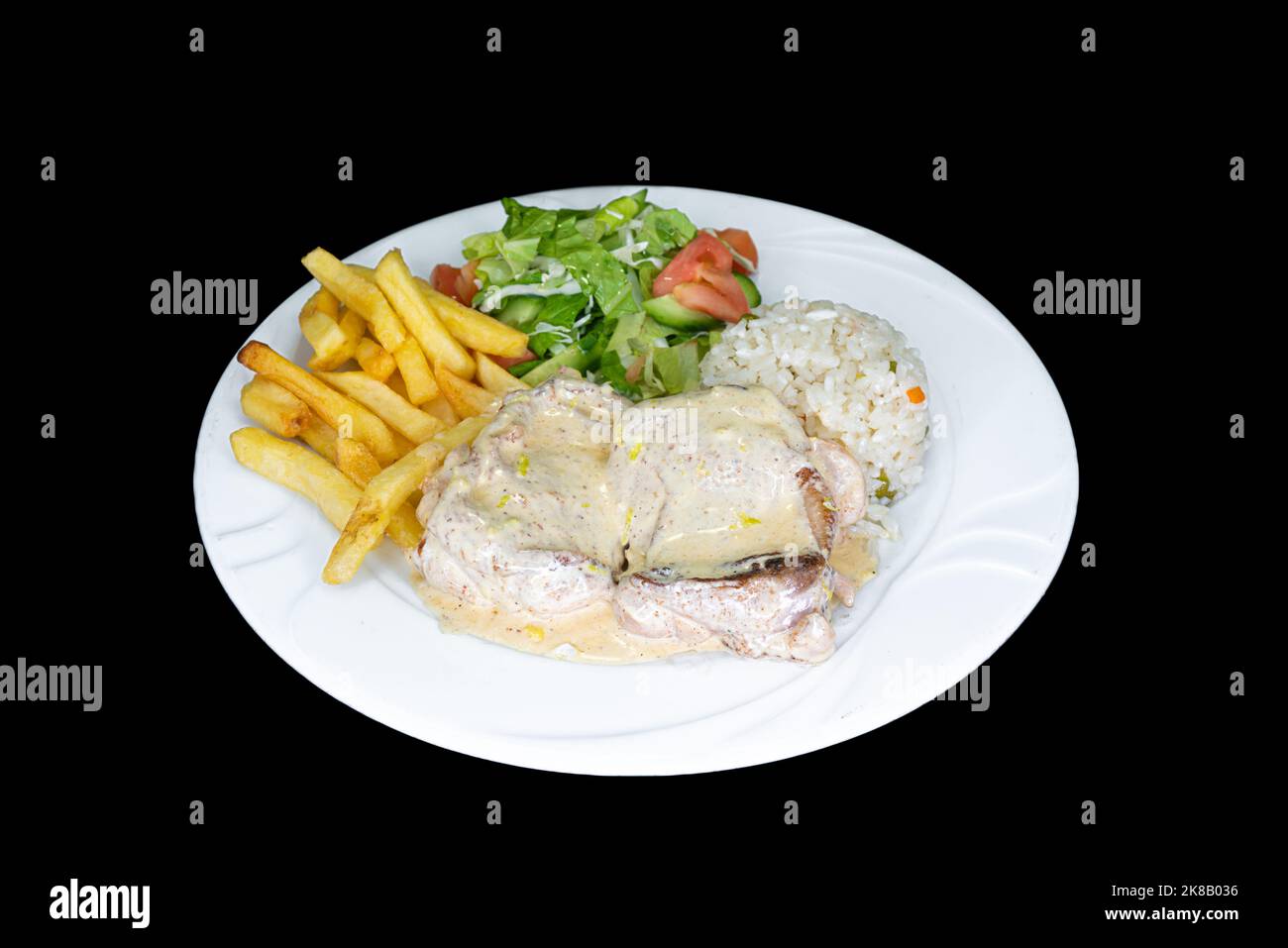 Lemon chicken with rice, salad and french fries in a white plate on a black background Stock Photo