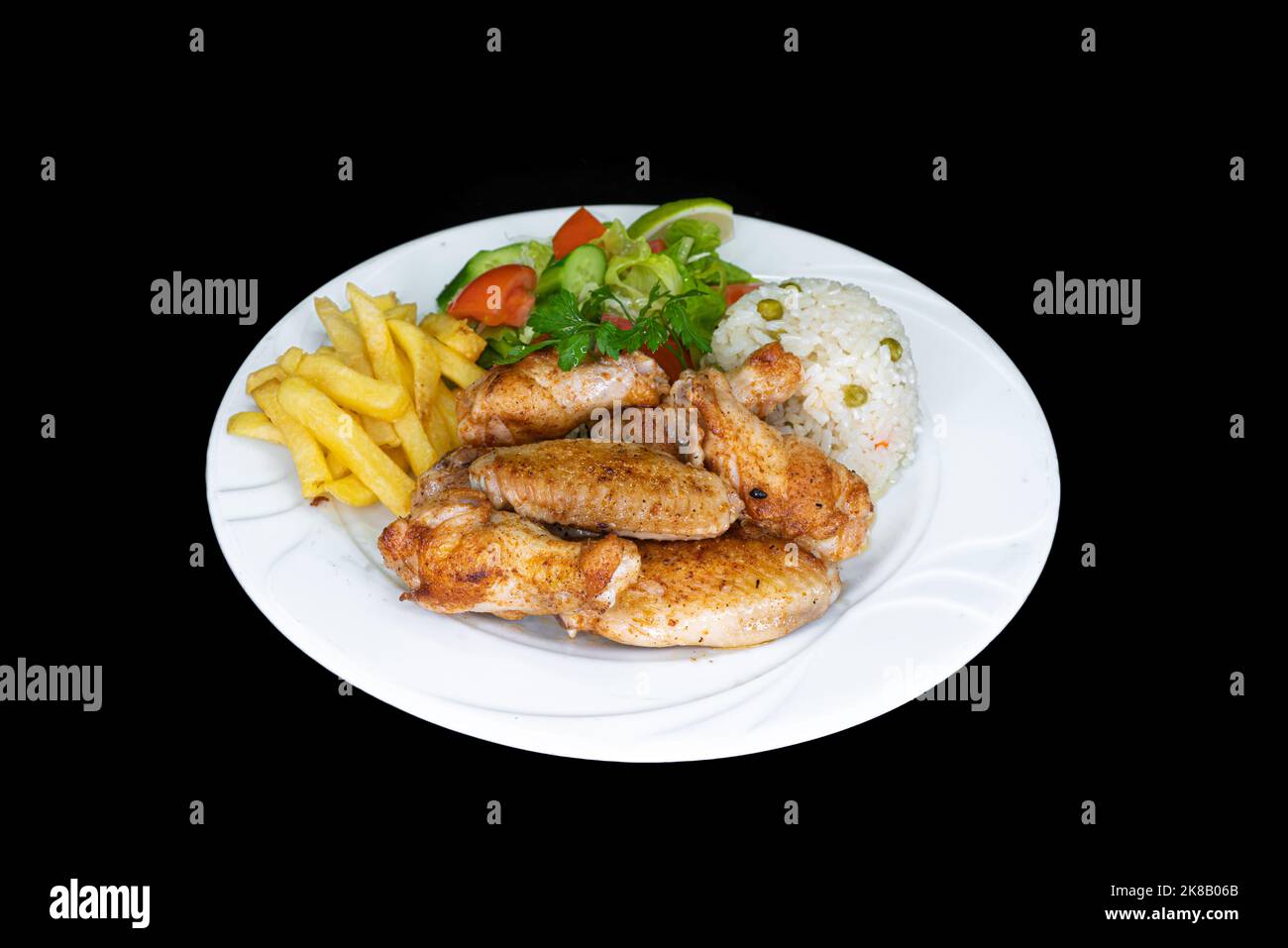 Grilled chicken wings with rice, salad and french fries in a white plate on a black background Stock Photo