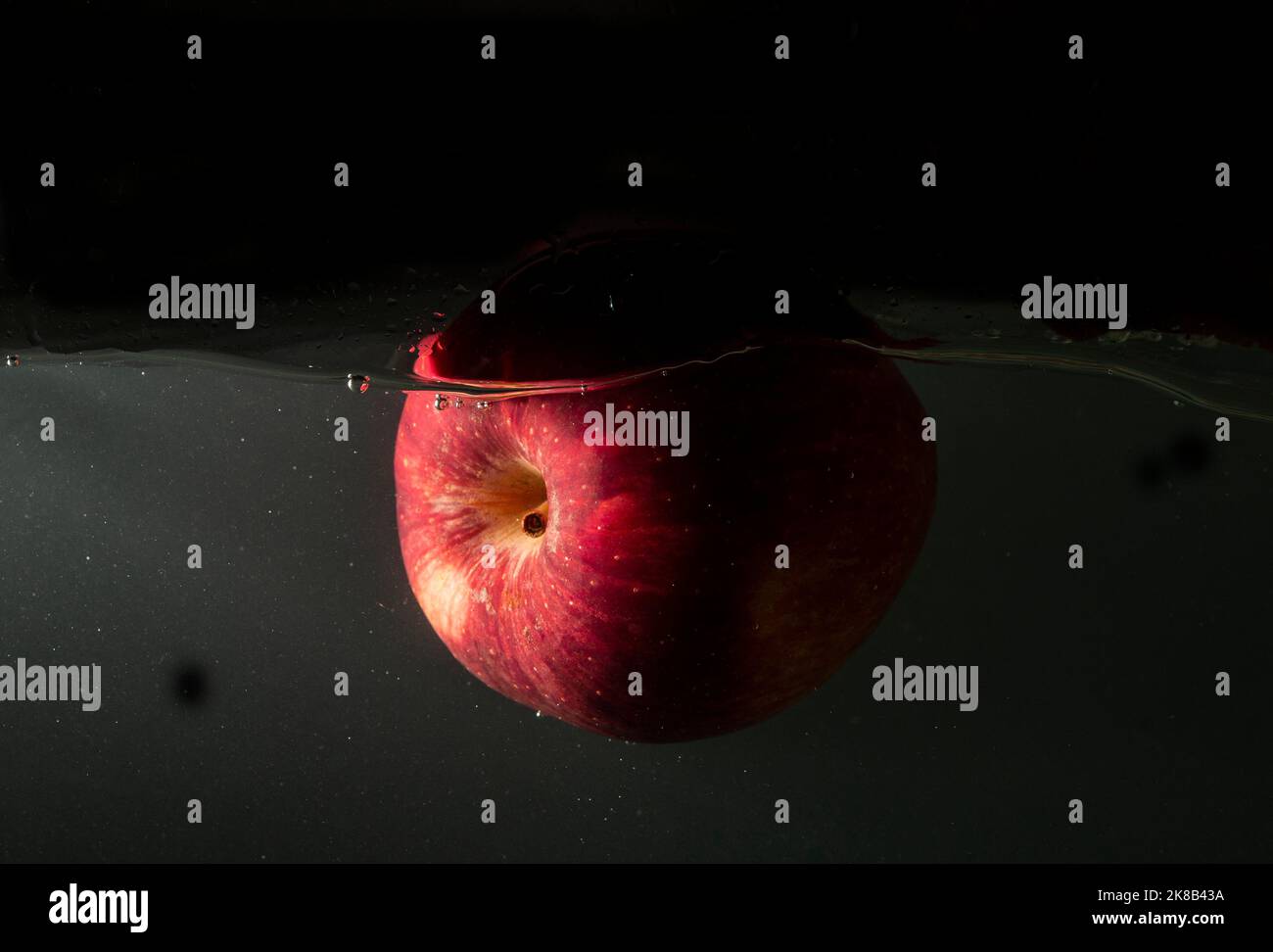 Red apple floating inside the water with dark background. Stock Photo