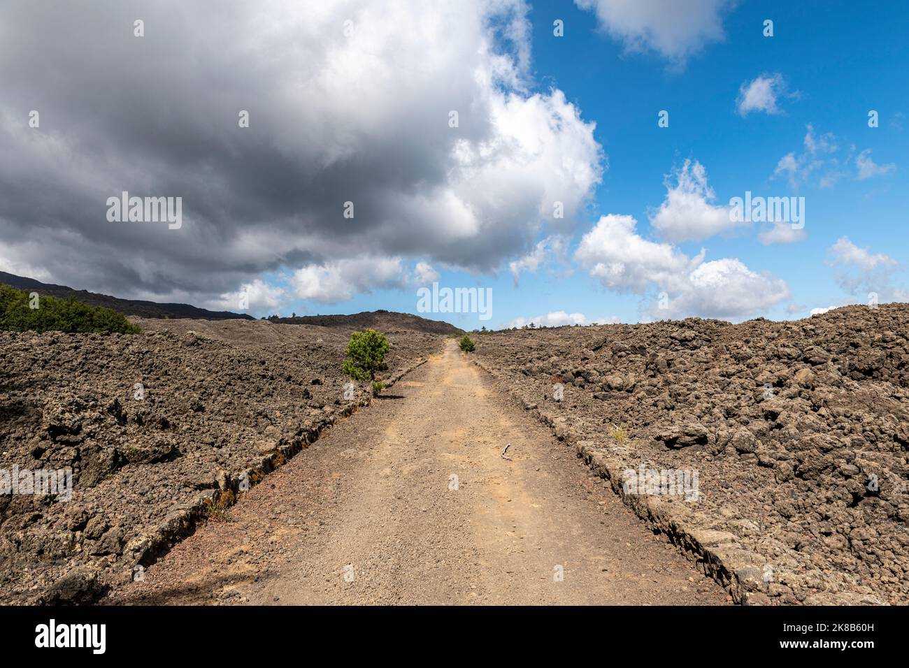 A long-distance hiking trail and forestry track crosses the harsh terrain of an old lava flow high on the slopes of Mount Etna, Sicily Stock Photo