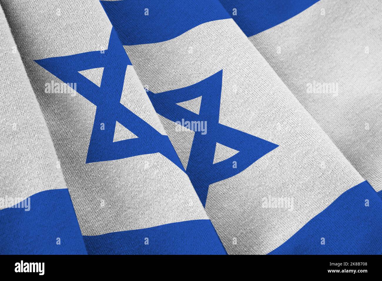 Israel flag with big folds waving close up under the studio light indoors. The official symbols and colors in fabric banner Stock Photo