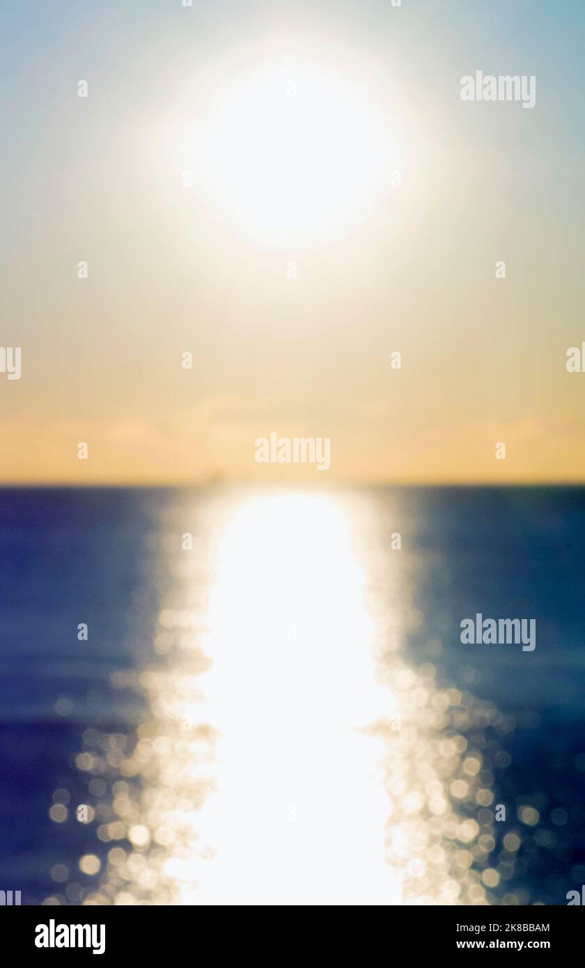 Blurred background. Sun shining in sky during sunset dawn. Sunrise dawning sundown. Sunny path, sunny walkway on of sea blue waves. Sunlight. Sea landscape. Natural blurry bokeh texture. Vertical Stock Photo