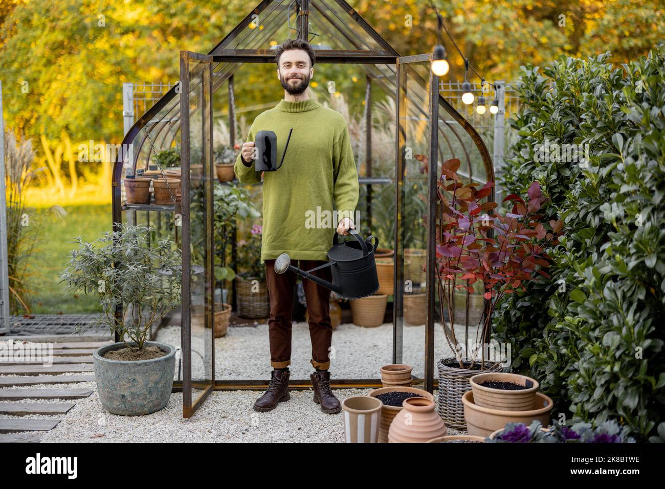 Stylish guy with watering can in garden Stock Photo