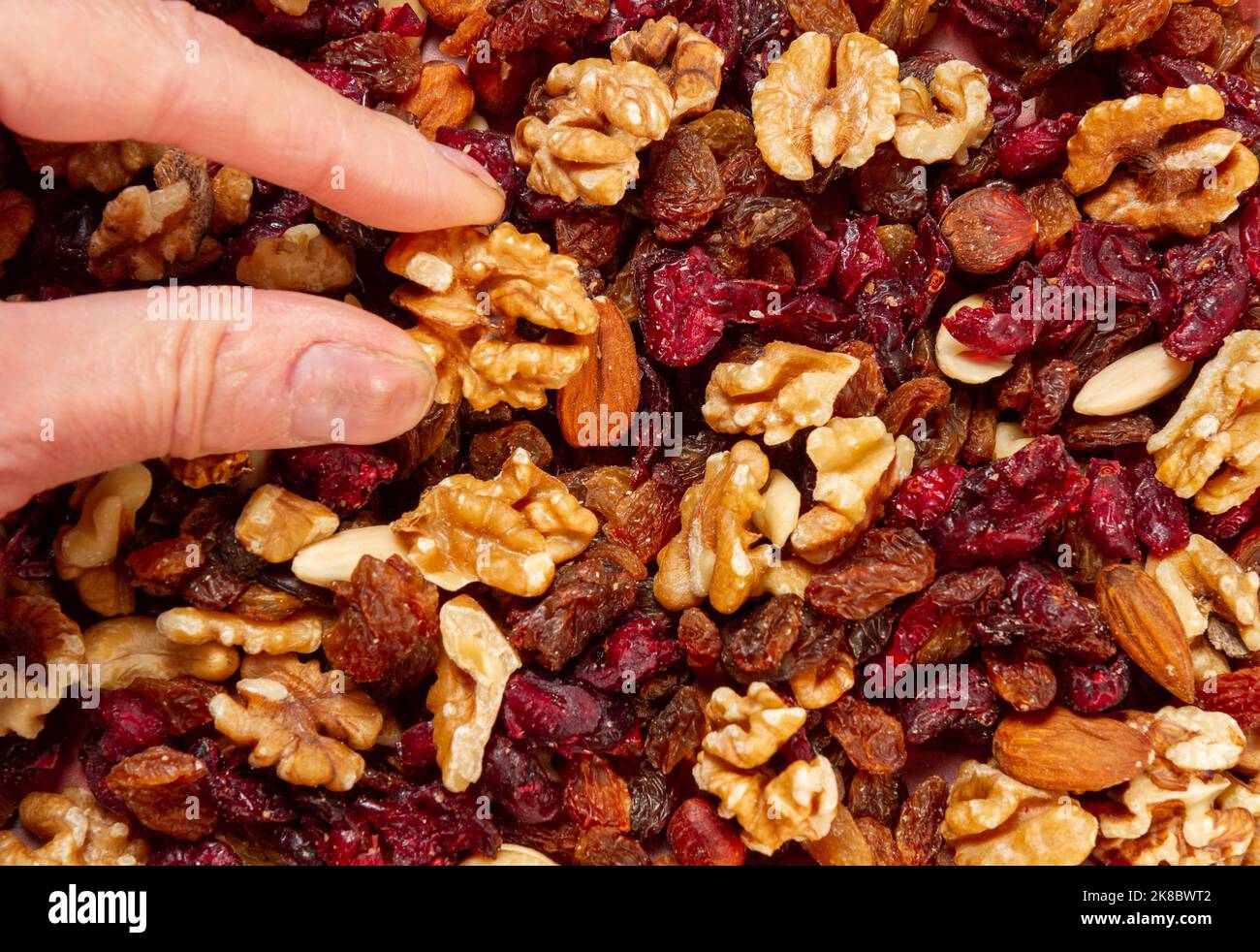 fingers picking up walnut from fruit and nut mix Stock Photo