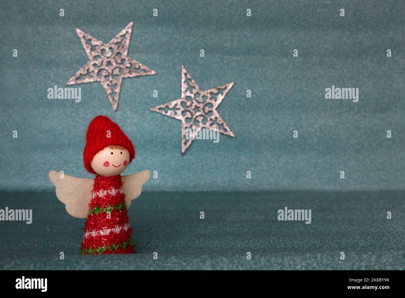 A cute Christmas angel figurine with white wings wearing a red hat and clothes isolated against a glittering pastel blue background with a star Stock Photo