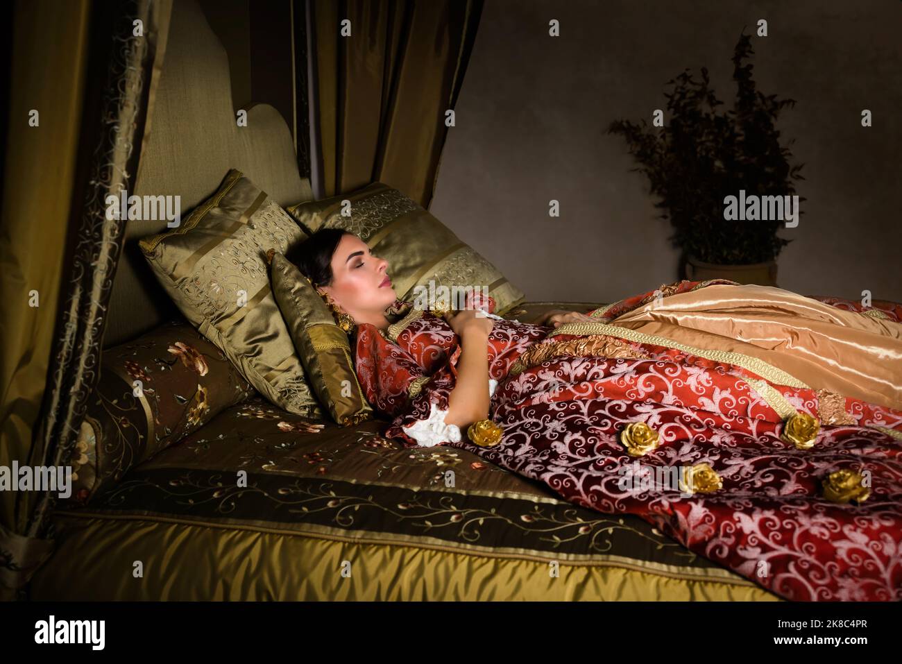 Golden medieval bedroom with beautiful canopy bed. A lady in renaissance dress lying on it in