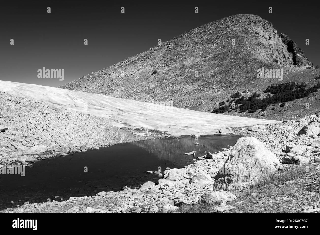 A small alpine pond lying among rocks below snow and the Paintbrush