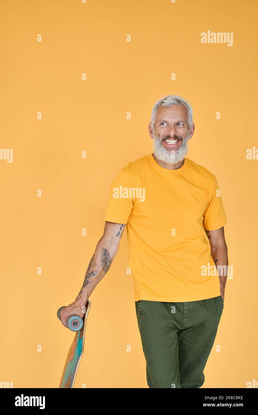 Happy cool old senior man skater holding skateboard isolated on yellow. Stock Photo