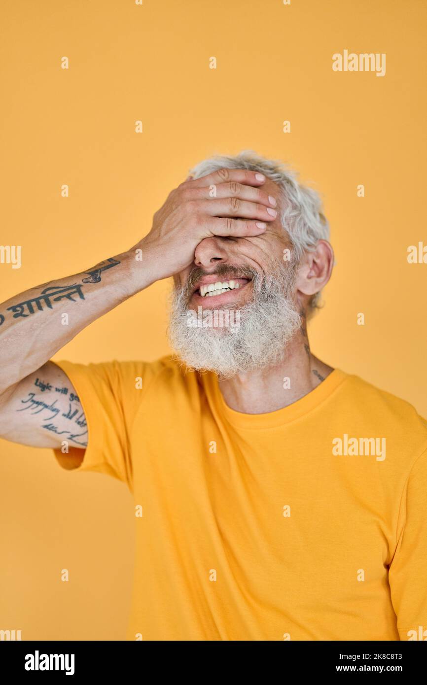 Smiling funny older bearded tattooed man laughing isolated on yellow. Stock Photo
