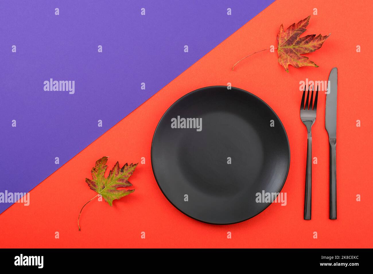 Autumn table place setting with black plate on orange and purple background. Thanksgiving, halloween decoration. Top view, flat lay, copy space Stock Photo