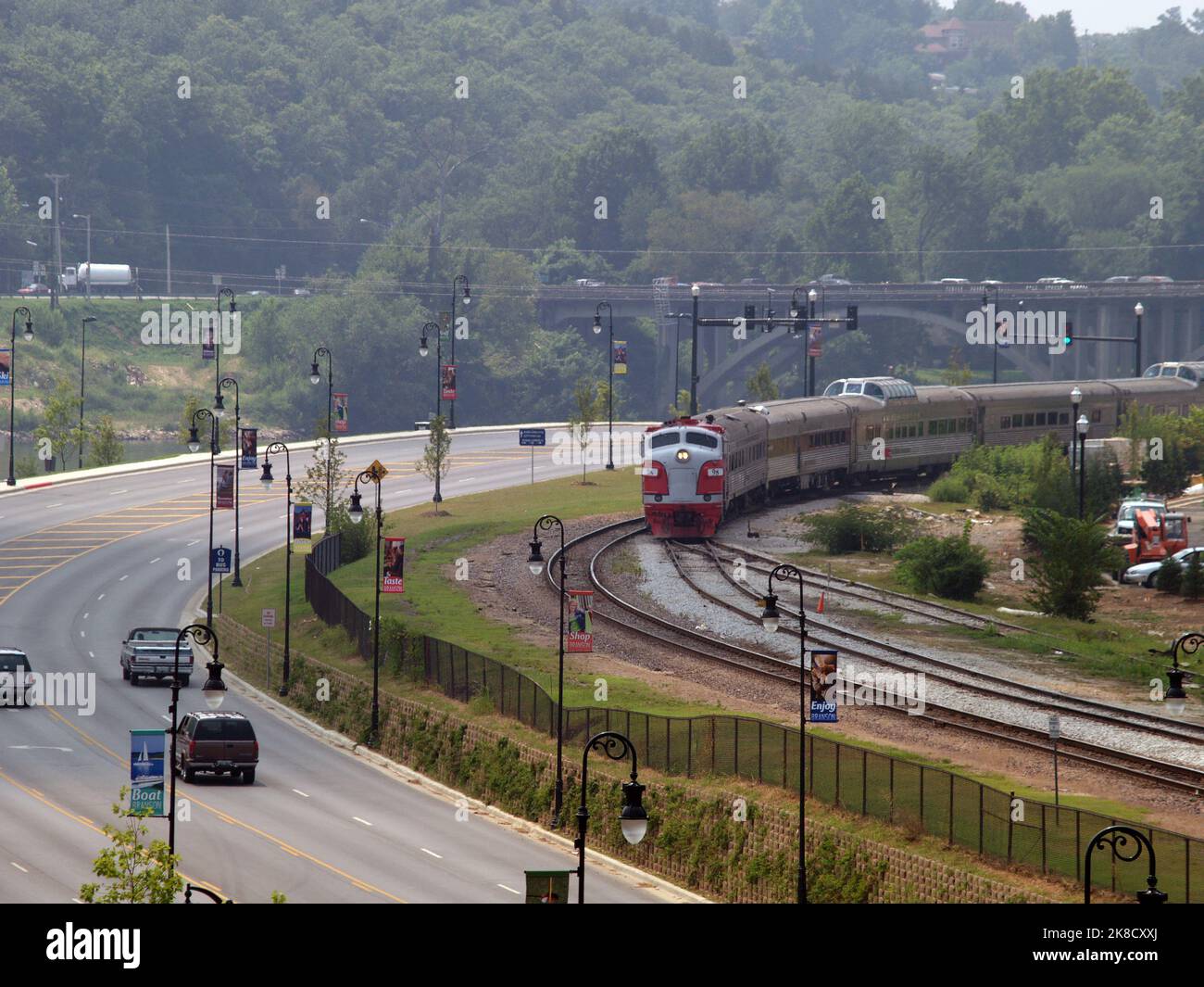 The Branson Scenic Railway Train rounds the bend coming into Branson, Missouri. Branson Landing Blvd. runs parallel to the tracks along the waterfront Stock Photo