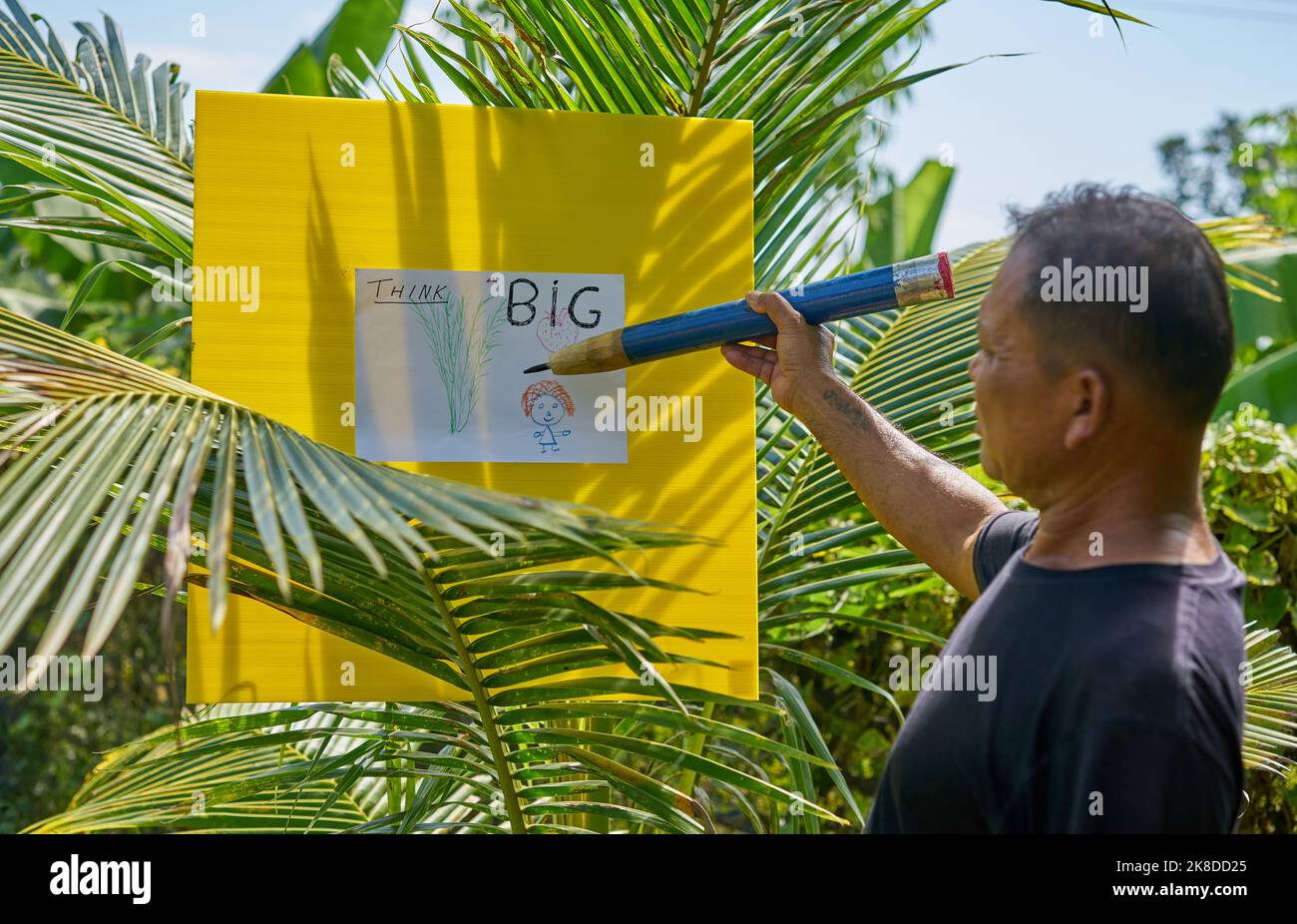An artist drawing in a tropical garden using a very large pencil. Stock Photo