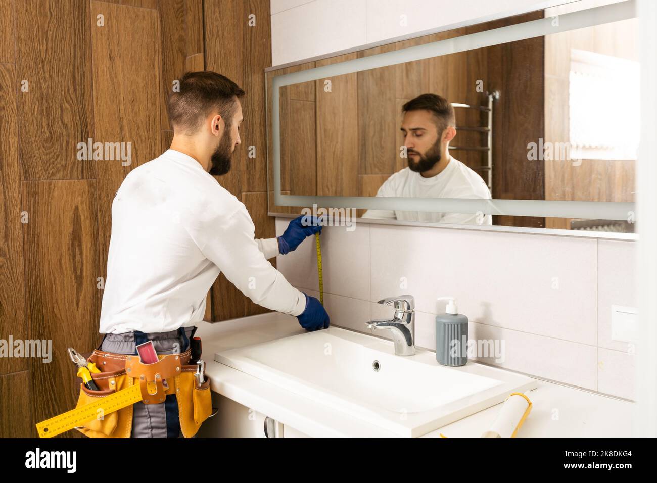 The worker installs the mirror in the bathroom Stock Photo Alamy