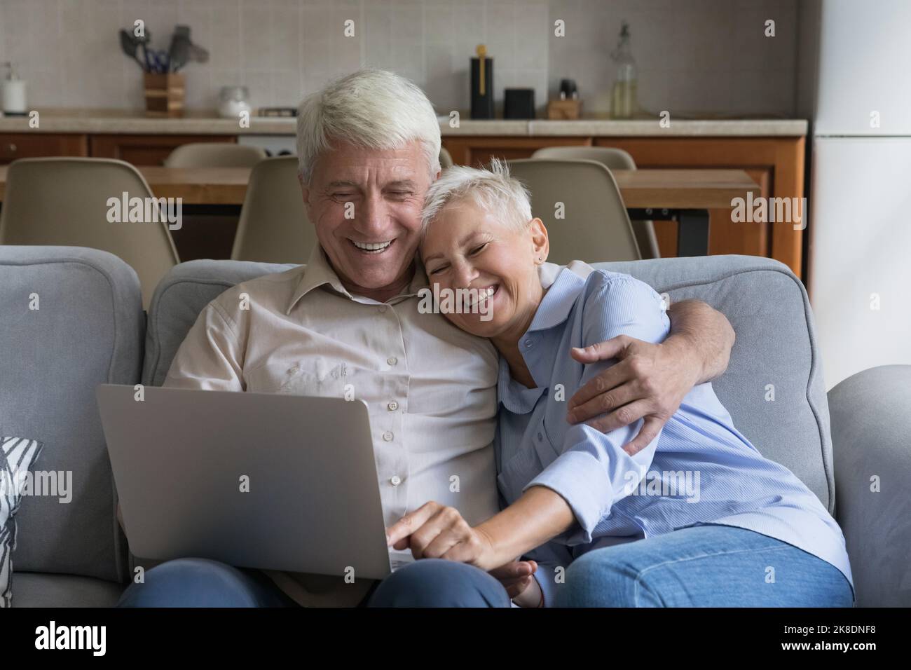 Happy older spouses relaxing on sofa at home using laptop Stock Photo