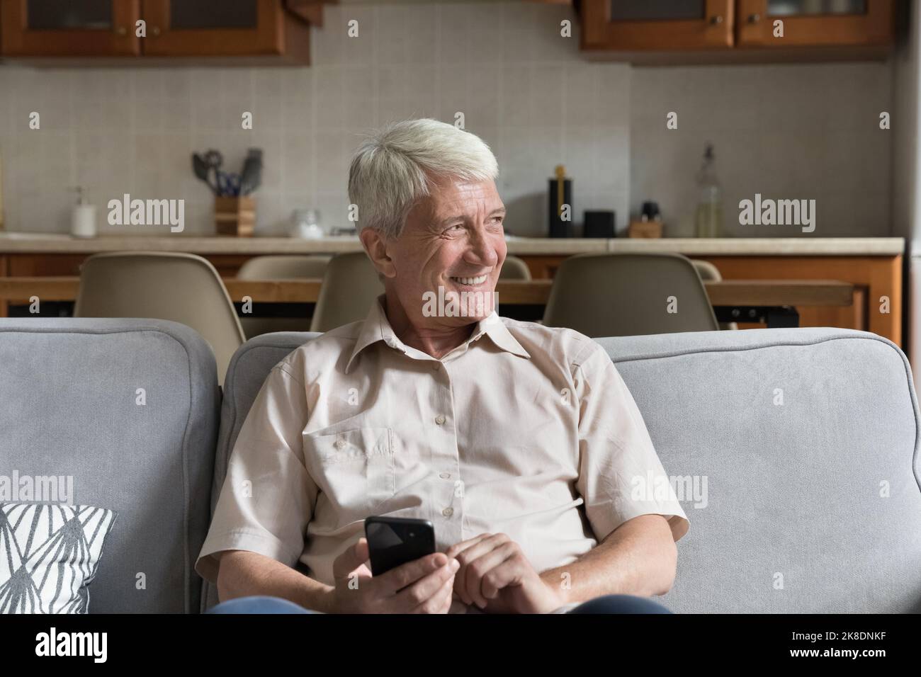 Mature single man sits on sofa with modern smartphone Stock Photo