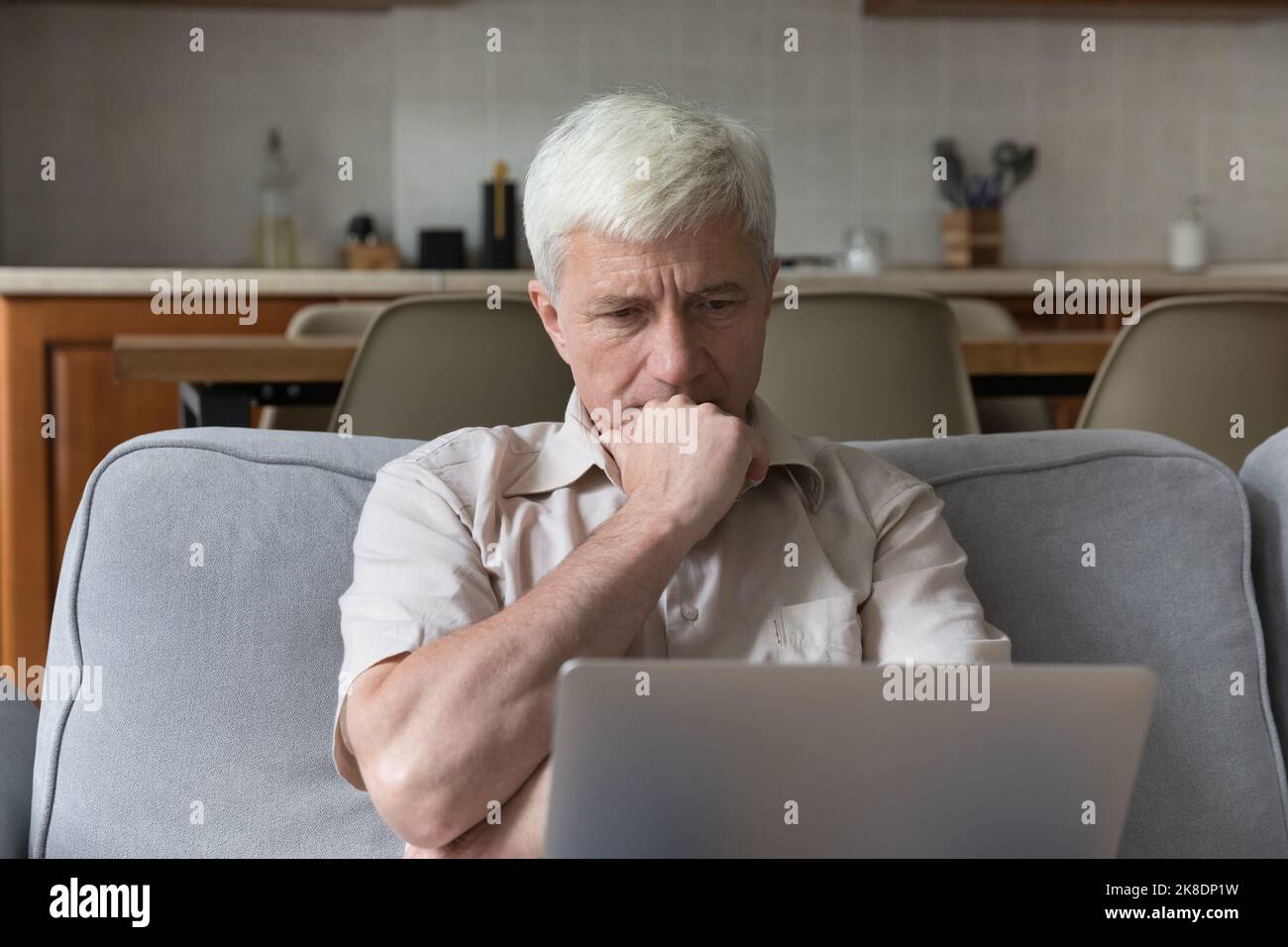 Serious thoughtful older man sit on couch with laptop Stock Photo