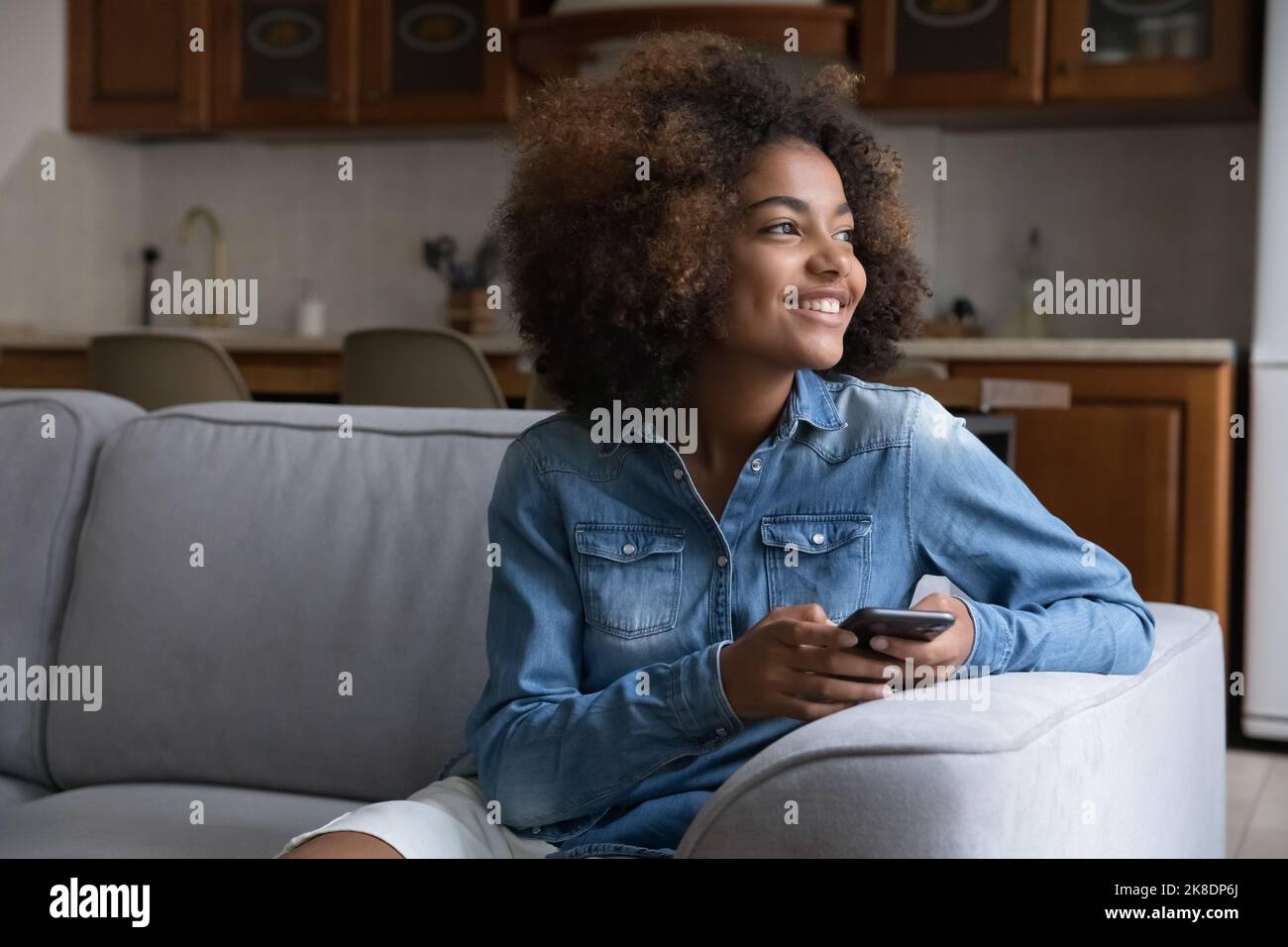 Beautiful African teenager girl resting on sofa with smartphone Stock Photo