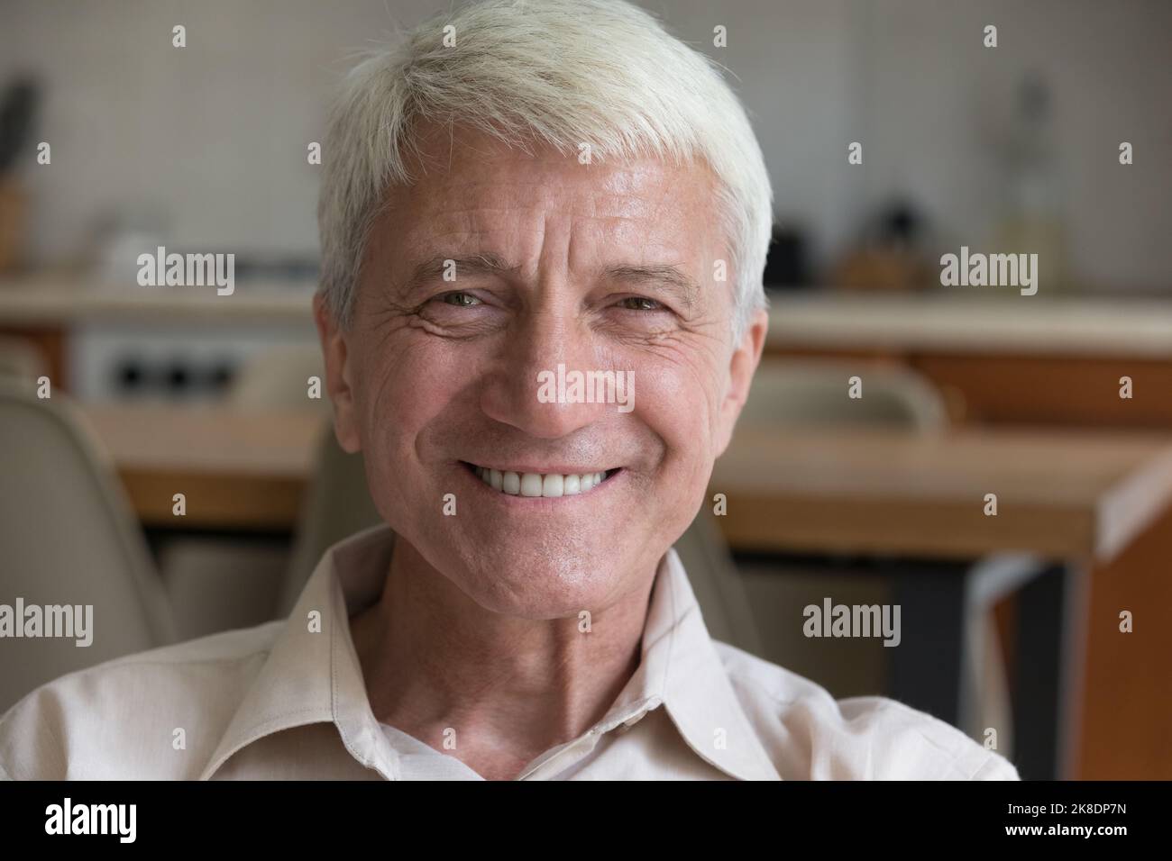 Happy older man sits indoors looking at camera Stock Photo