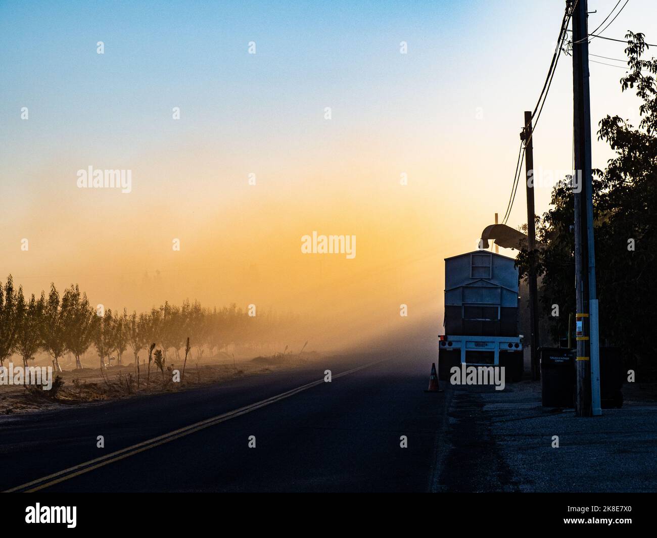Early morning, the sun rises, a truck waits to be filled with a harvest of walnuts as dust from the machinery creates a large cloud of dust. Modesto Stock Photo