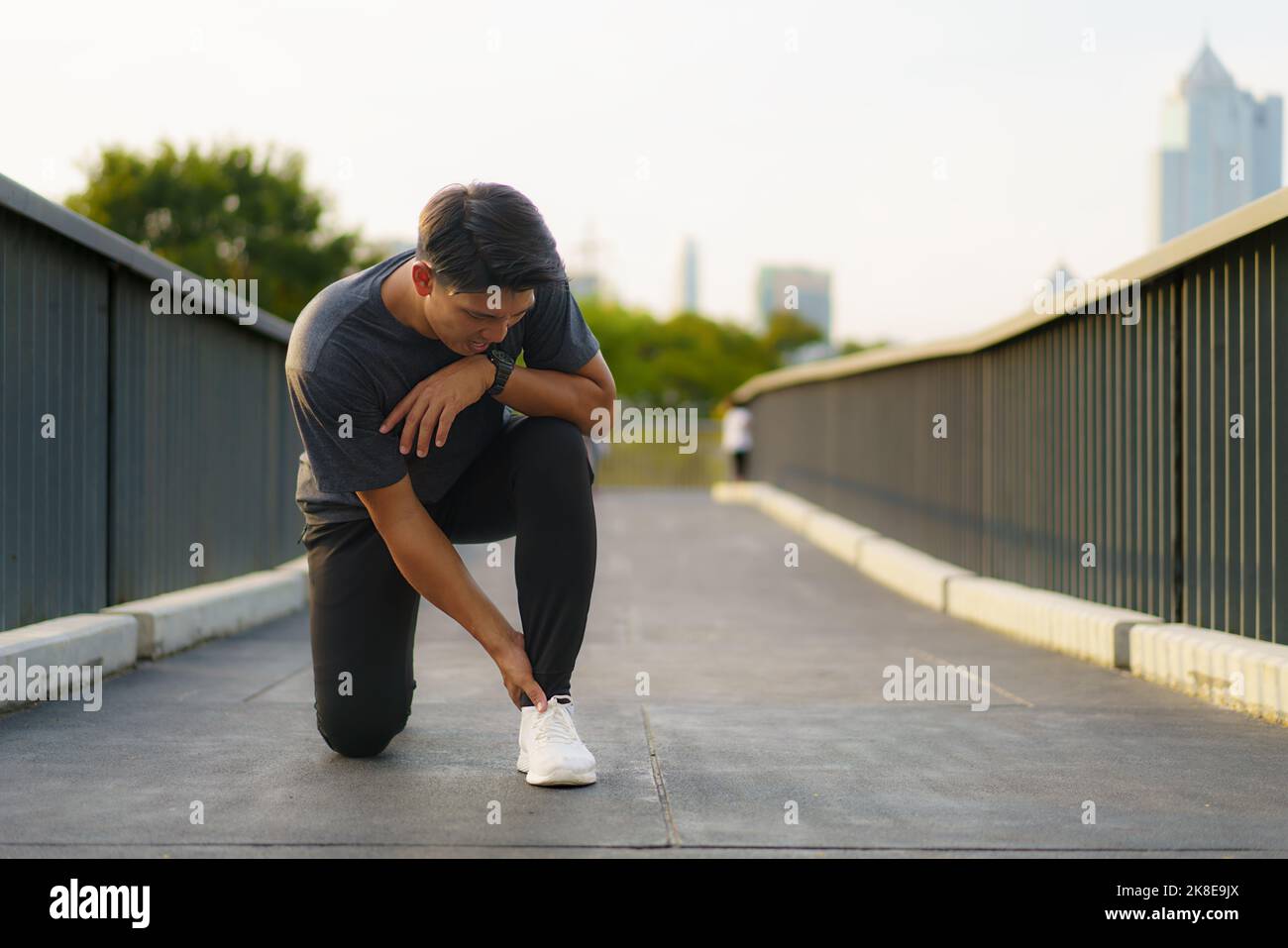 Asian Runner suffering ankle injury after sport outdoors in a city outskirts park Stock Photo