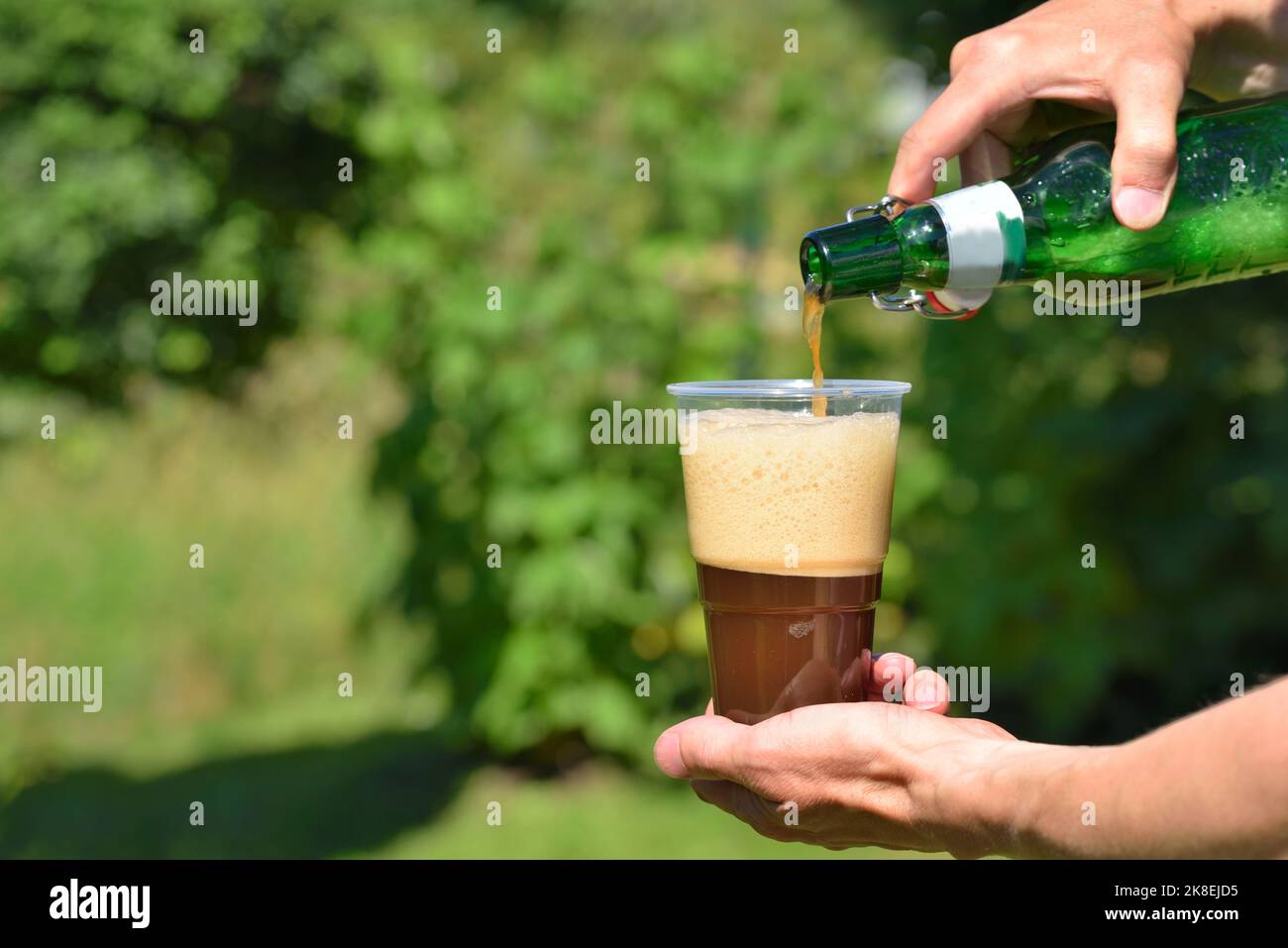 Hand pouring dark beer into a plastic glass Stock Photo - Alamy