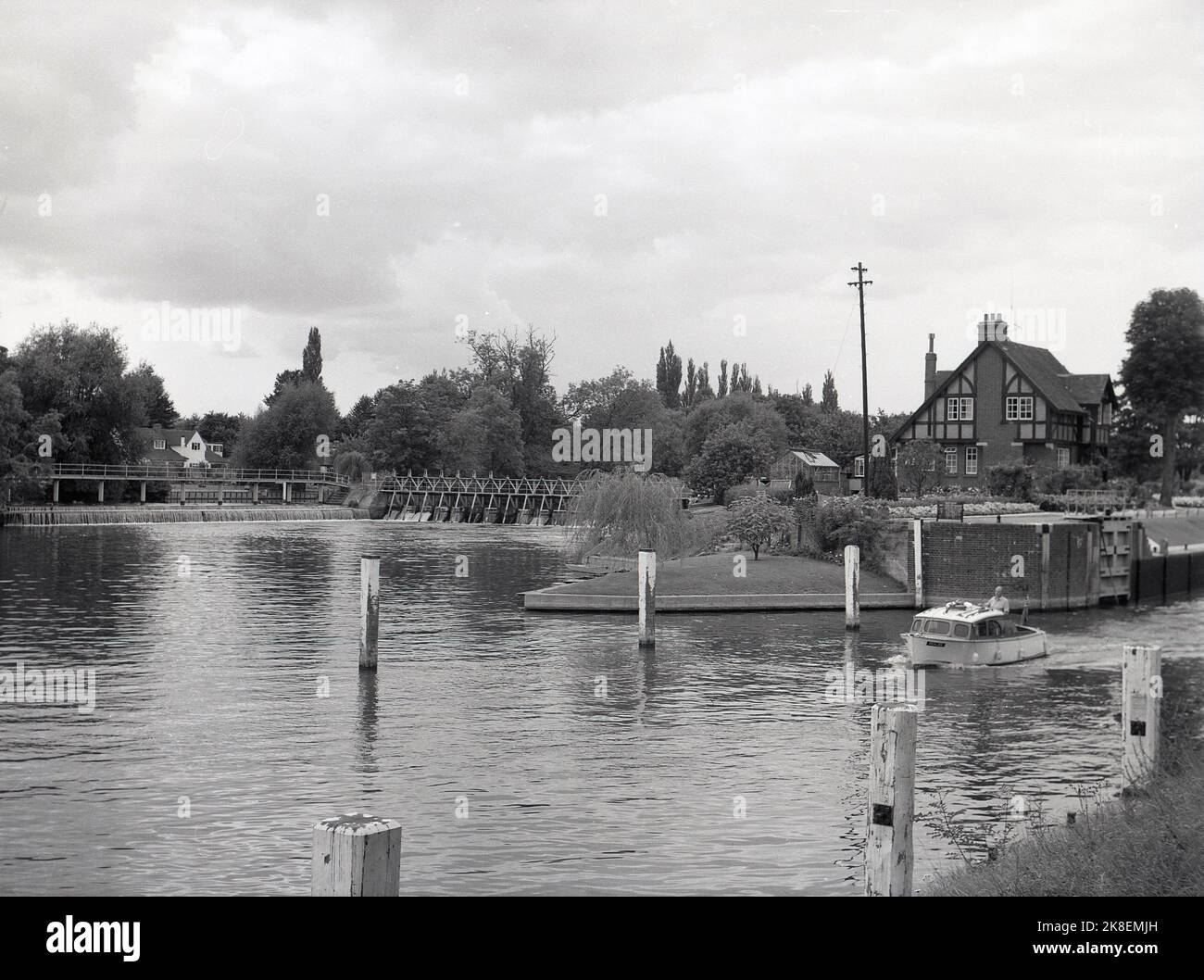 1962, historical, a small pleasure boat coming out of Bray lock, on the river Thames. Builtin 1845, the grass-sided lock is officially on the Buckinghamshire side the thames, although Bray itself is in Berkshire. Seen in the picture, the lock keeper's cottage which is located between the lock and weir. Stock Photo