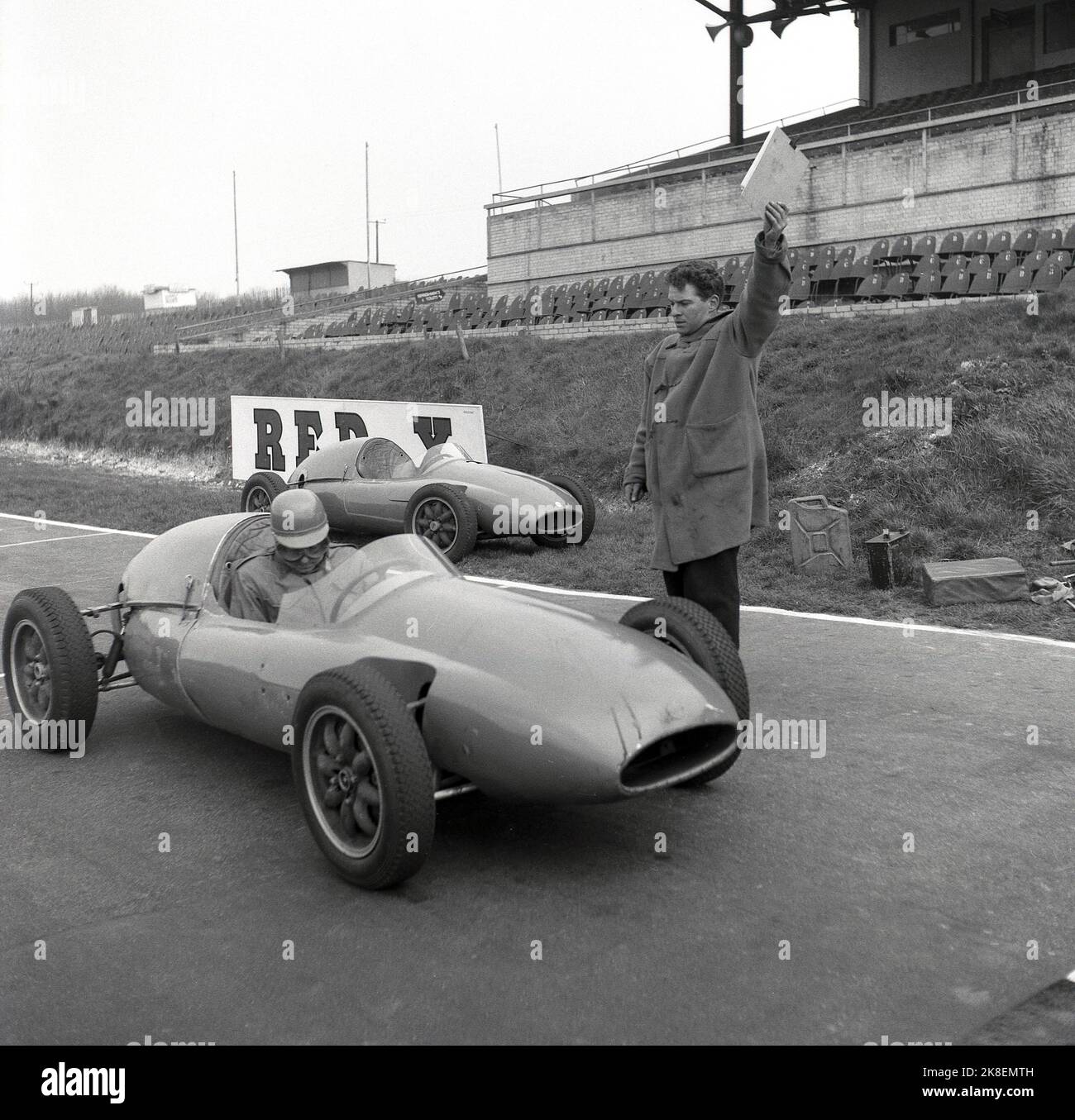 1959, historical, motor racing, Cooper Driving School, a racing driver in an open top, single-seater, a Formula Cooper Junior. on the race track at Brands Hatch, Kent, England, UK, about to start.  Official standing by car holding a small clip board. A legendary name in motor sport, Coopers reached the highest level becoming Formula One Constructor World Champions in 1959 & 1960, the first ever winners in a rear-engined car. At this time, the British based Cooper Car Company was the world’s largest specialist manufacturer of racing cars and their 'Mini Cooper' led the way in Stock Photo