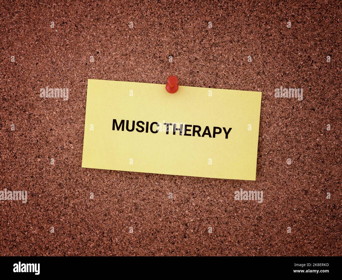 A yellow paper note with the words Music Therapy on it pinned to a cork board. Close up. Stock Photo