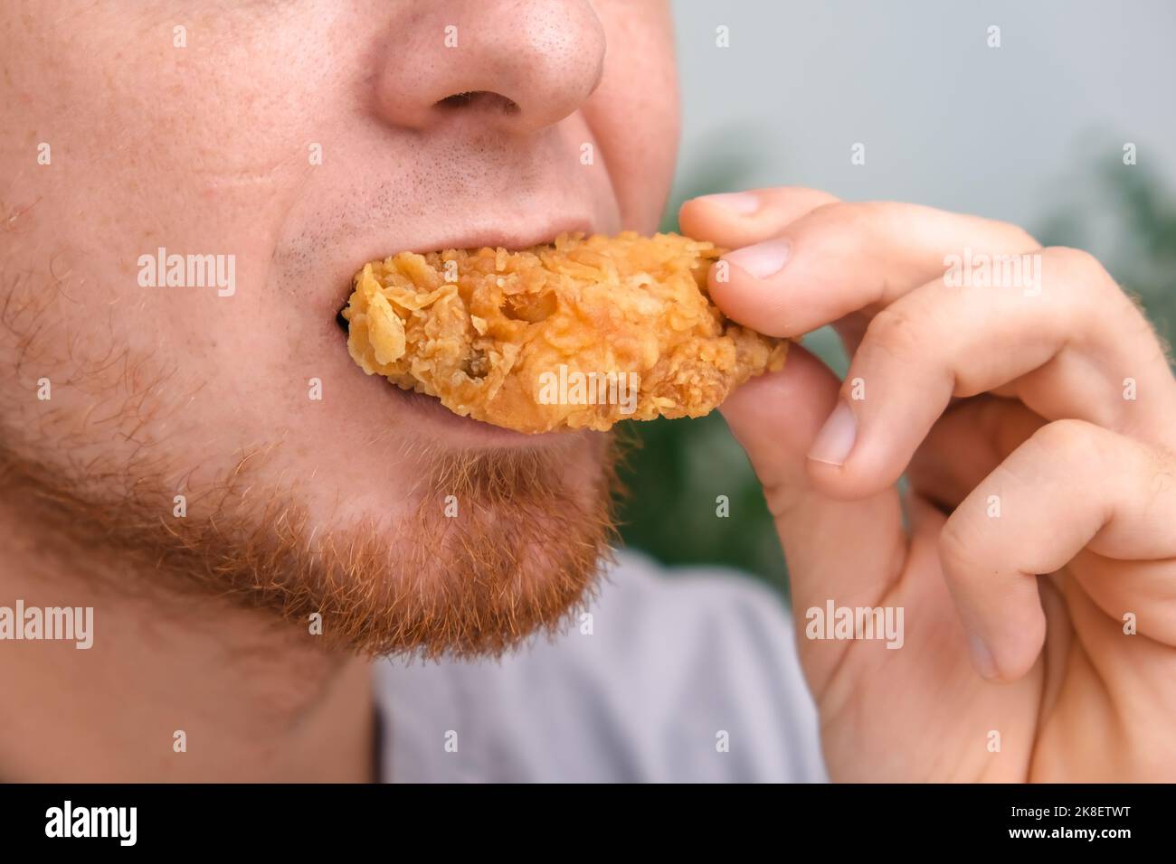 A man bites and chews a fried chicken wing in breadcrumbs. A man eats