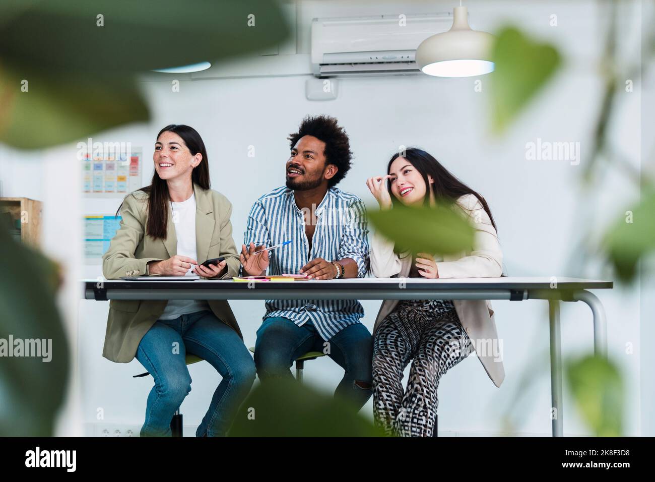 Three colleagues at table in office looking sideways Stock Photo