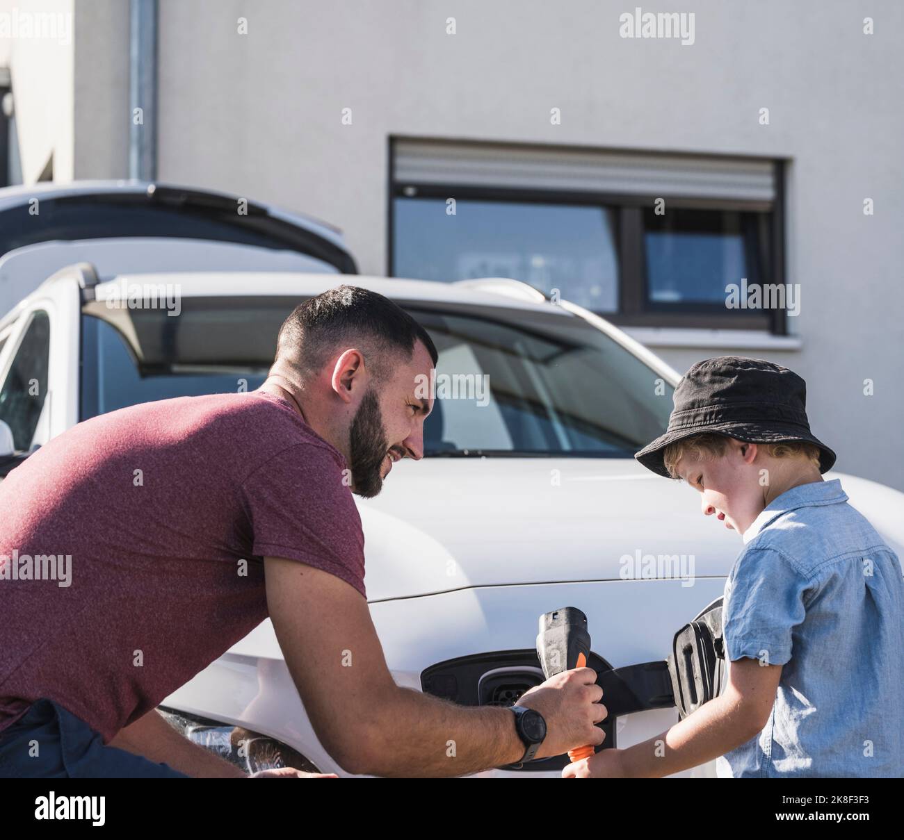 Father and son charging electric car in front of residential house Stock Photo