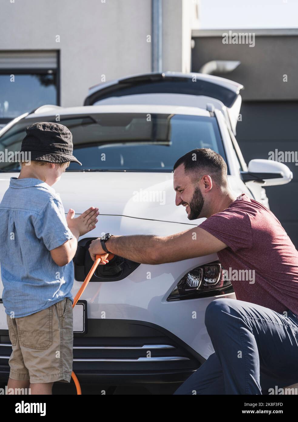 Father and son charging electric car in front of residential house Stock Photo