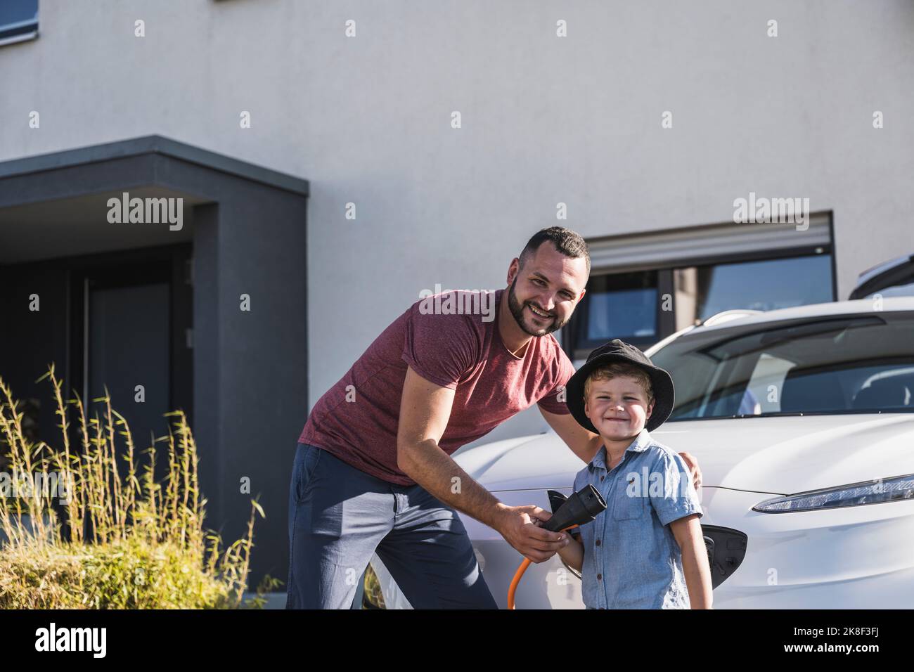 Father and son charging electric car in front of residential house Stock Photo