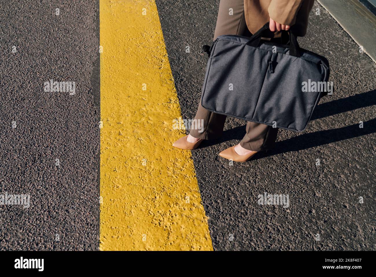 Businesswoman with laptop bag standing by yellow line on road Stock Photo