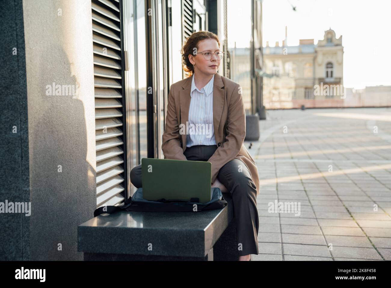 Thoughtful young freelancer with laptop sitting on bench Stock Photo