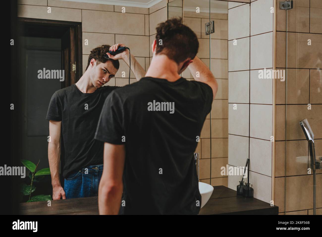 Young man with electric razor cutting his hair in bathroom Stock Photo